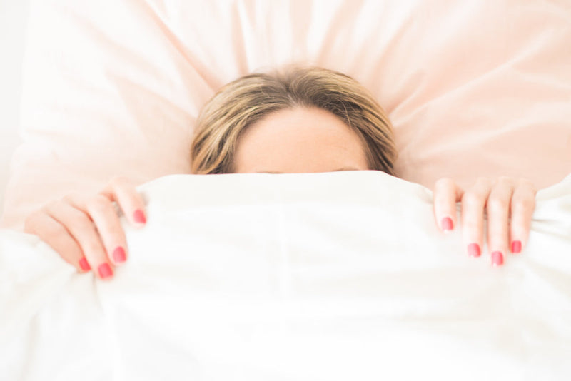 Woman peeking over the duvet in bed